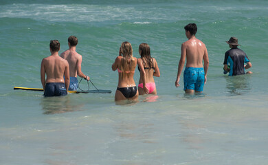 A group of teenagers wait for breaking waves at the beach.