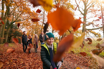 Children Throwing Leaves As Multi-Generation Family Walk Along Autumn Woodland Path