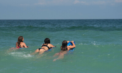 3 teenage girls ride waves on boogie boards in the ocean