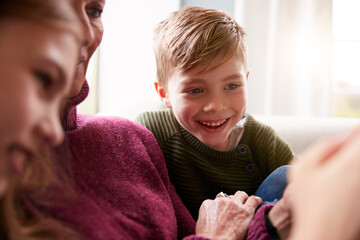 Grandchildren On Sofa At Home Showing Grandmother How To Use Mobile Phone