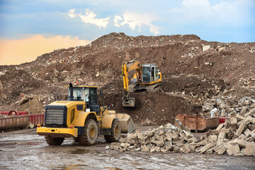 Front end loader and excavator at landfill for disposal of construction waste. Gravel and concrete...