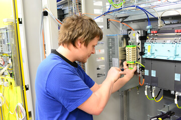 young apprentice assembles components and cables in a factory in a switch cabinet - workplace...