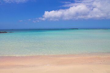 Beach with pink sand and turquoise water and clouds in blue sky.