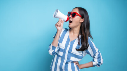 Beautiful woman wearing red glasses in blue modern fashion clothe holding megaphone and shouted in...