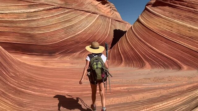 A hiker walking through the sandstone rock formations of The Wave in Arizona. Slow-motion wide follow shot from behind.