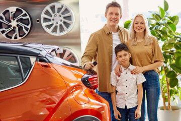 happy young caucasian family now the owners of new beautiful car, they made purchase in cars dealership, get keys from it