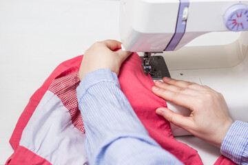 Girl sews on a sewing machine. Modern white sewing machine. White and pink fabric. Sewing content.