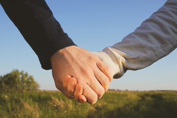 Man and woman hold hands on a background of green trees. In the frame only hands close-up. The concept of love, romance, relationship, being together, walking.
