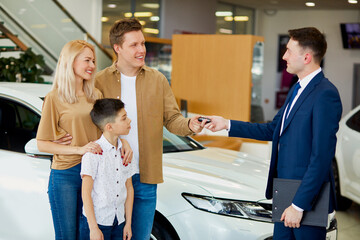 adorable family get keys by car in dealership, affable confident consultant give long-awaited keys to clients