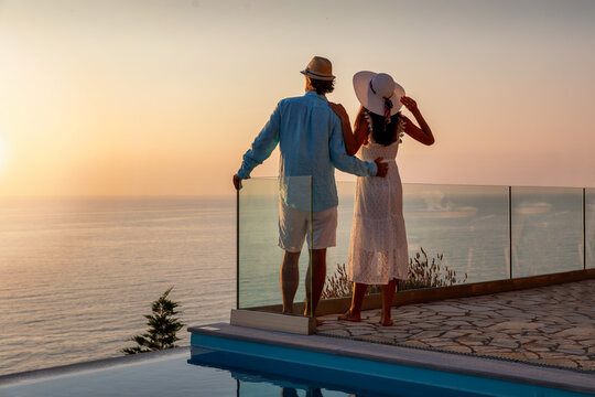 Romantisches Paar im Sommerurlaub steht am Pool und genießt den Sonnenuntergang über dem Meer