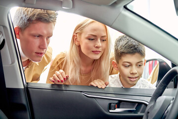 young caucasian family look inside of car, inspecting it before purchase. boy with parents in love with this car, want to buy it