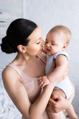 attractive mother looking at infant son in baby romper