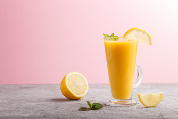 Glass of lemon drink on a gray and pink background. Side view