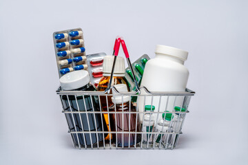 Shopping basket cart full of pills and medical supplies over light grey background