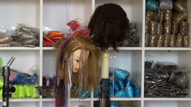 Strands of artificial and natural hair are on the shelves in the store. Mannequin heads in wigs for sale