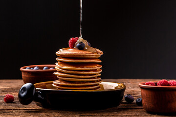 Pouring honey on stack of tasty pancakes on wooden table. homemade classic american pancakes with...