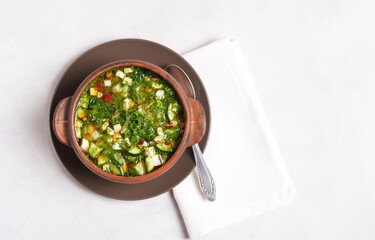 Russian summer okroshka with bread kvass is standing in a clay cup on a gray background, top view, horizontal orientation, there is a mine of space.