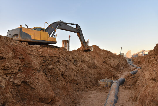 Excavator Dig The Trenches At A Construction Site. Trench For Laying External Sewer Pipes. Sewage Drainage System For A Multi-story Building. Civil Infrastructure Pipe, Water Lines And Sanitary Storm