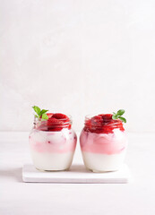 Homemade yogurt with ripe strawberries decorated with mint stands in banks on a wooden stand on a gray background. Vertical orientation, there is a place for copying.