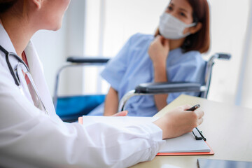 Beautiful young Asian female doctor is recording a medical history on the clipboard and explaining something to the female patient. Medical and health care concepts