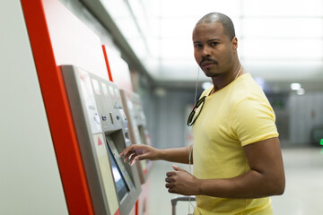 Young latino man purchasing ticket at terminal in subway platform