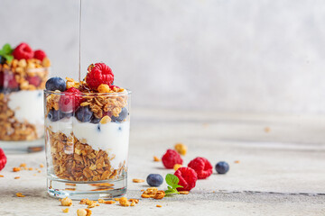 Yogurt parfait with granola, raspberries, honey and blueberries in glasses, light gray background,...