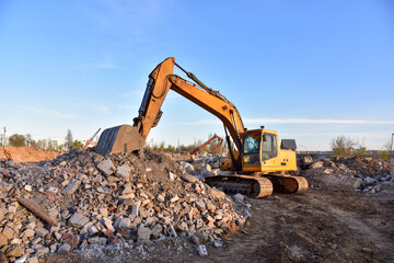 Obraz premium Excavator work at landfill with concrete demolition waste. Salvaging and recycling building and construction materials. Industrial waste treatment plant. Reuse concrete for new construction