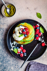 Matcha tea pancakes with berries, dark background, top view. Healthy vegan food concept.