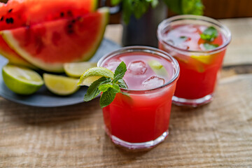Watermelon smoothie lemonade with lime, topping with fresh mint leaves for the summer drinks concept. Homemade refreshing cold drink on wooden rustic table near window. Selective focus, copy space.