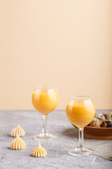 Sweet egg liqueur in glass with quail eggs and meringues on a gray and orange background. Side view