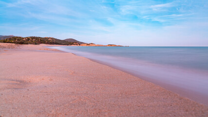 Panoramic view of a long exposure sunset shot of Su Giudeu beach, in Chia, Cagliari, Italy, with seashore view, mountains and soft waves