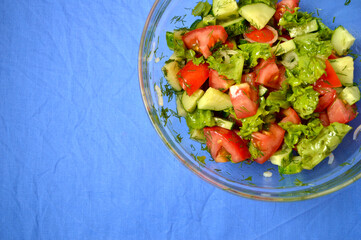 Salad of tomatoes, cucumbers, onions, lettuce with sunflower oil in a glass bowl on a blue background
