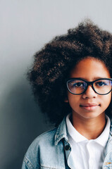 Half a portrait of a dark-skinned girl near a gray wall.