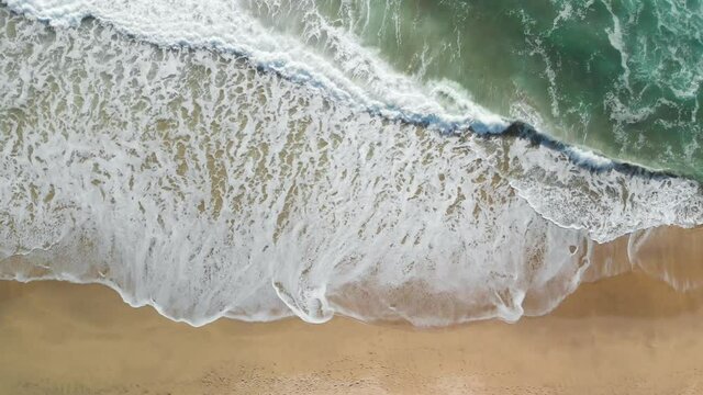 Top-down aerial shot of the blue ocean waves crashing on the California shore near Montara.