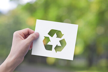 Environment concept. Hand holding white paper with recycle symbol on green bokeh background.