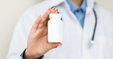 Physician medicine doctor or pharmacist sitting at worktable, holding or showing bottle of pills in hand and writing prescription on special form. Medical care, pharmacy or health insurance concept