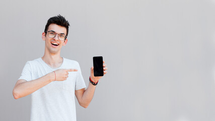 Portrait of a cheerful young man wearing casual clothing isolated over grey background, showing blank screen mobile phone