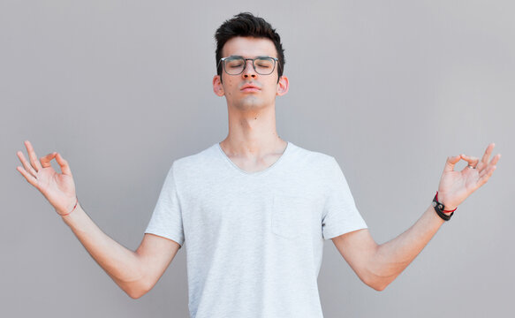 Concentrated relaxed man standing with closed eyes, having relaxation while meditating, trying to find balance and harmony. Yoga and meditation concept