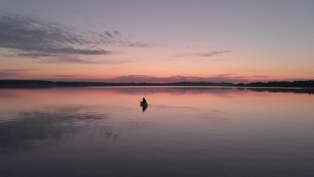 AERIAL Mid 50s Caucasian male canoeing on a traditional wooden boat on a large lake early in the morning. 4K UHD sunset shot