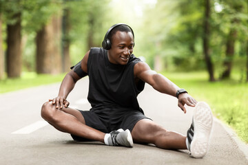 Black guy sportsman sitting on park path, stretching