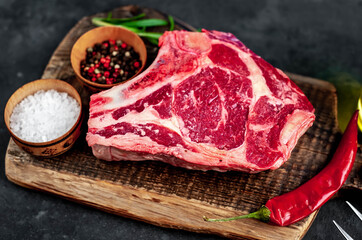 Raw cowboy steak. Marbled beef meat 
with spices on a stone background