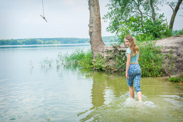 In the summer afternoon, a teenager girl stands in a lake.