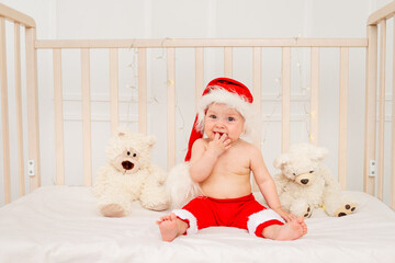 Obraz premium a small child is sitting in a crib in a Santa hat with stuffed toys bears, happy new year 2021, space for text