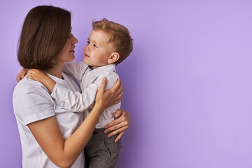portrait of sweet caucasian child boy with mother isolated over purple background. young mom and kid hugging, boy looks at mom with love