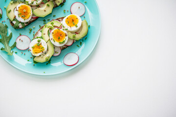 Sandwiches with soft boiled egg, avocado, radish, arugula, green onion and flax seeds on blue plate. Healthy snack.