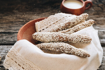 freshly baked fresh homemade breadsticks with sesame on clay plate with milk on a wooden table. Country food. Rustic style. top view.