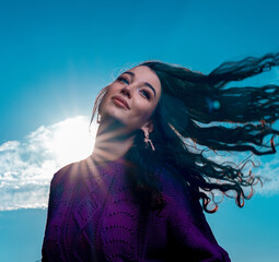 Happy Woman With Curly Fluttering in The Wind Hair at Blue Bright Sky Background. Summer Cotton Knitted Violet Sweater or Jumper