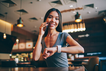 Portrait of brunette girl arranging meeting during phone conversation and checking time,young business woman organizing working day looking at camera talking on mobile spending time in coffee shop