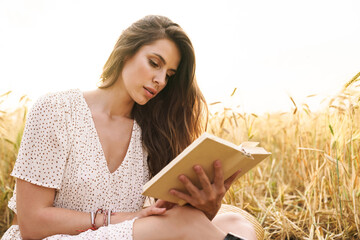 Photo of focused woman reading book while sitting on wheat field