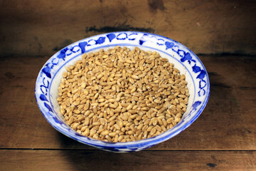 Pile of organic whole grain wheat. Fresh harvested wheat grain in a bowl isolated on wooden background. Wheat grains and wheat flour in wooden textured background. Food ingredient cereals concept.
